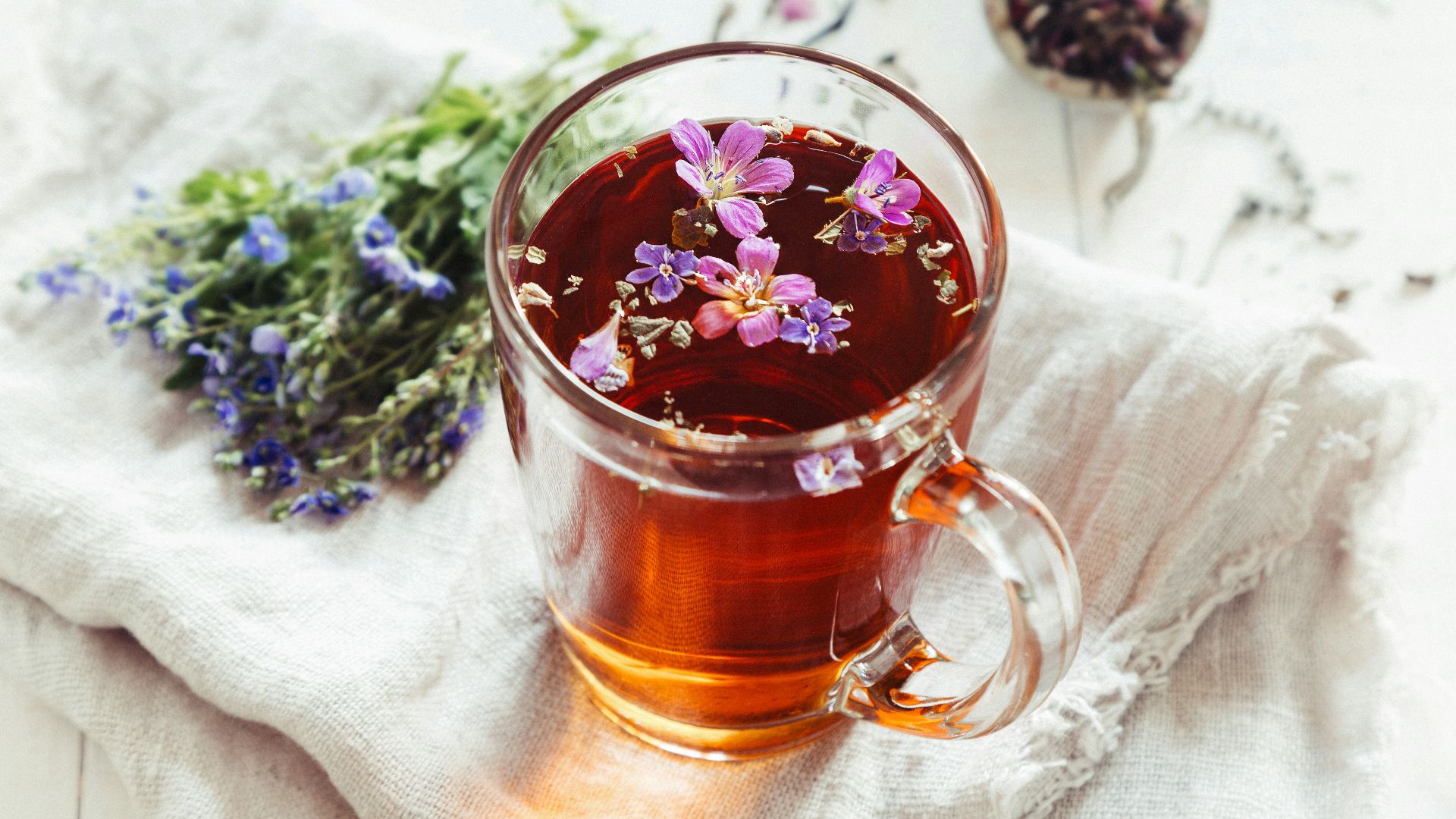 a glass mug filled with tea next to a bunch of flowers