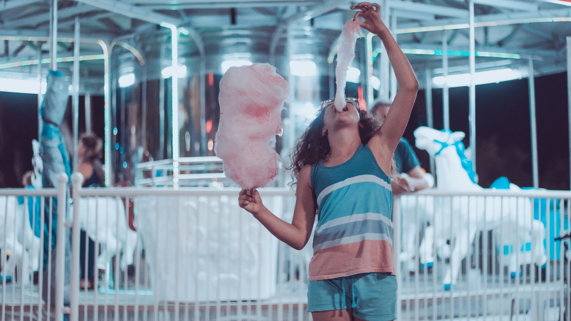 woman eating pink cotton candy beside carousel