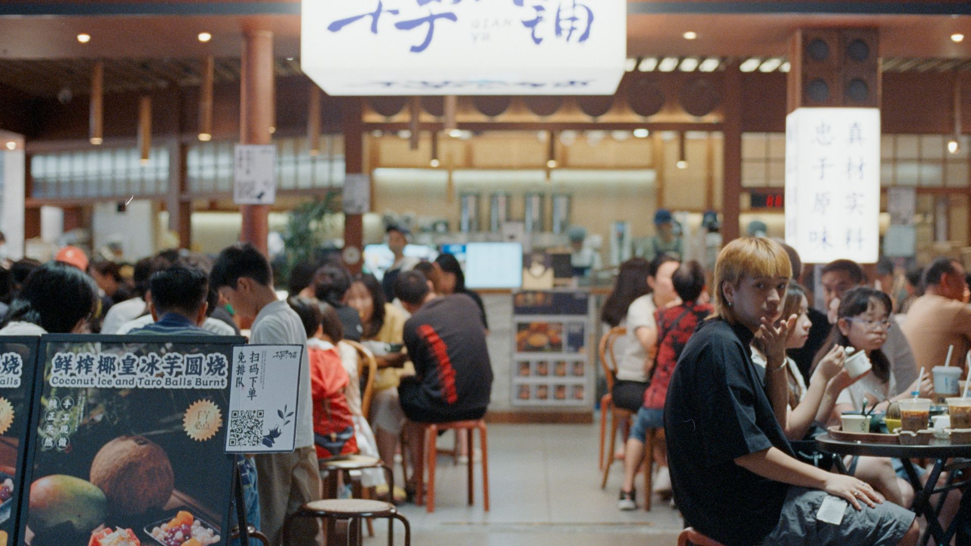 People eating at a busy food court with signs.