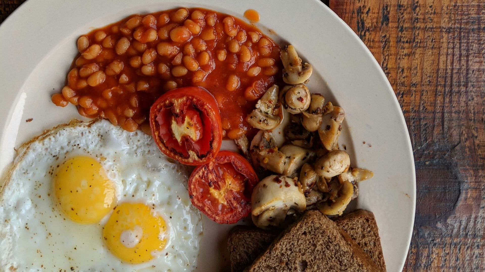 black coffee near sunny side up egg with sliced tomatoes, mushroom and bread on plate