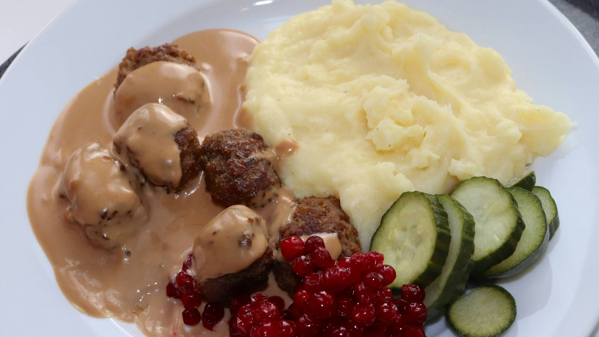 a white plate topped with meatballs, mashed potatoes and cucumbers