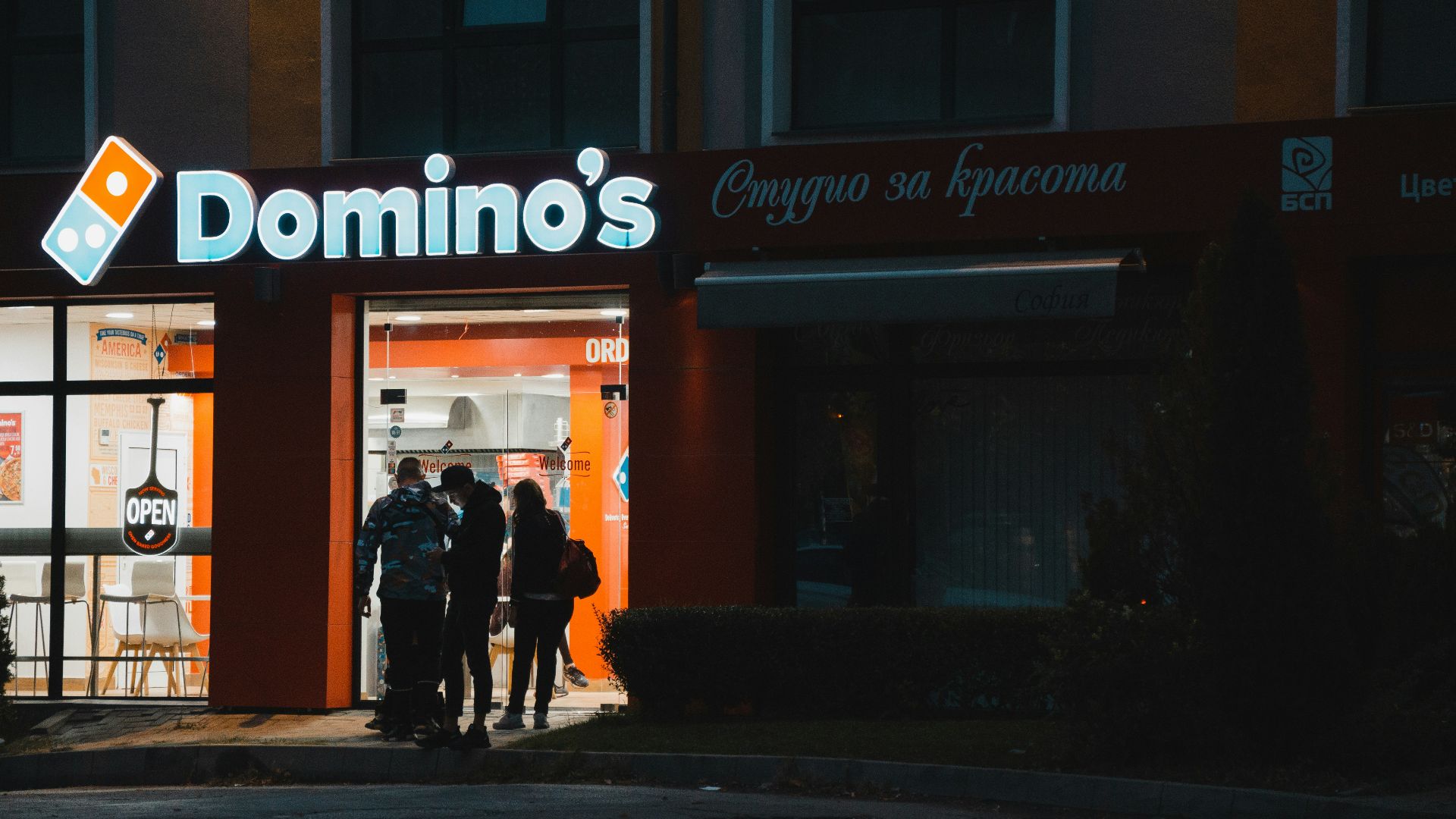 a group of people standing outside of a domino's store