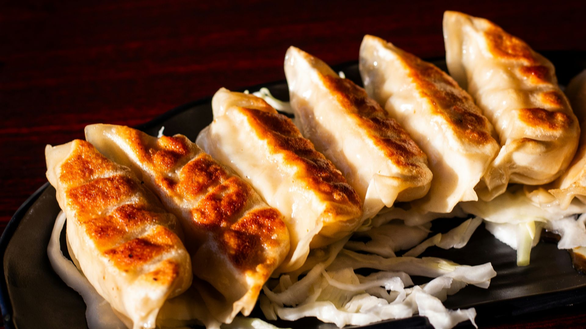A black plate topped with dumplings on top of a wooden table
