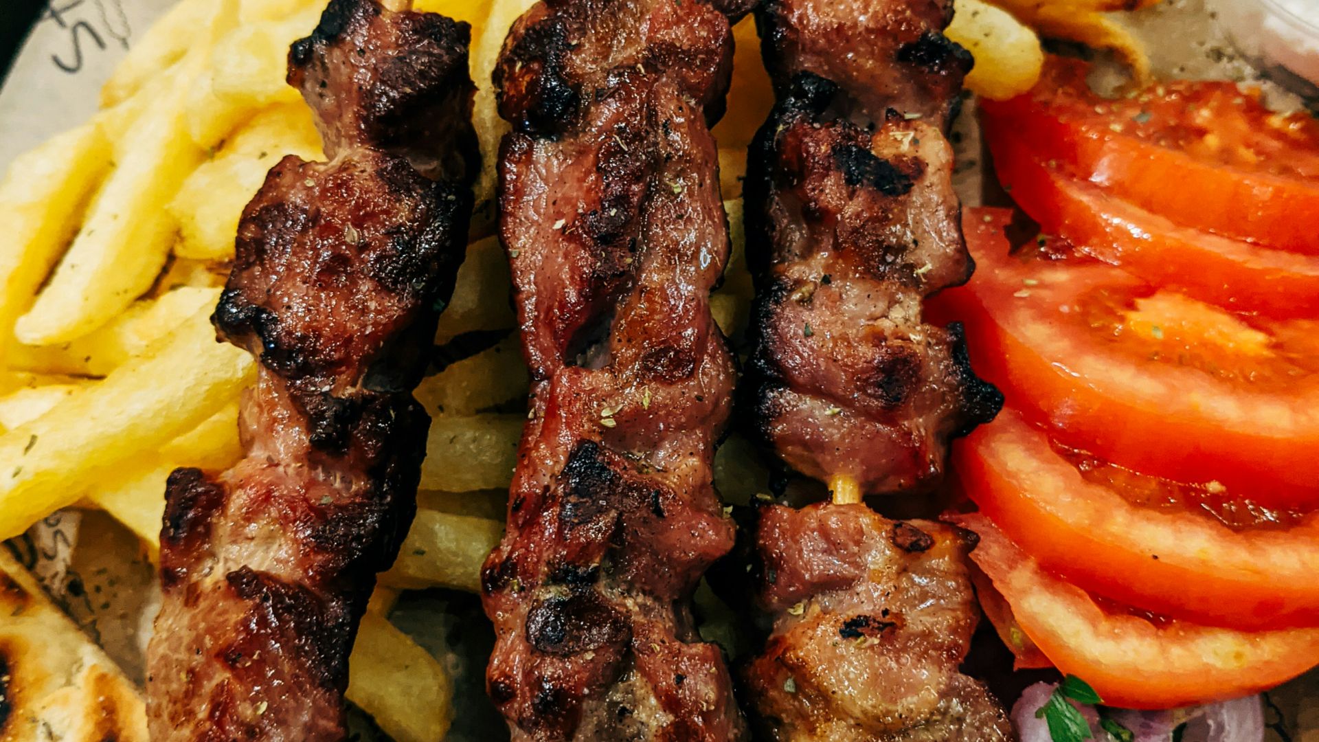 grilled meat with sliced tomato and green vegetable on white ceramic plate
