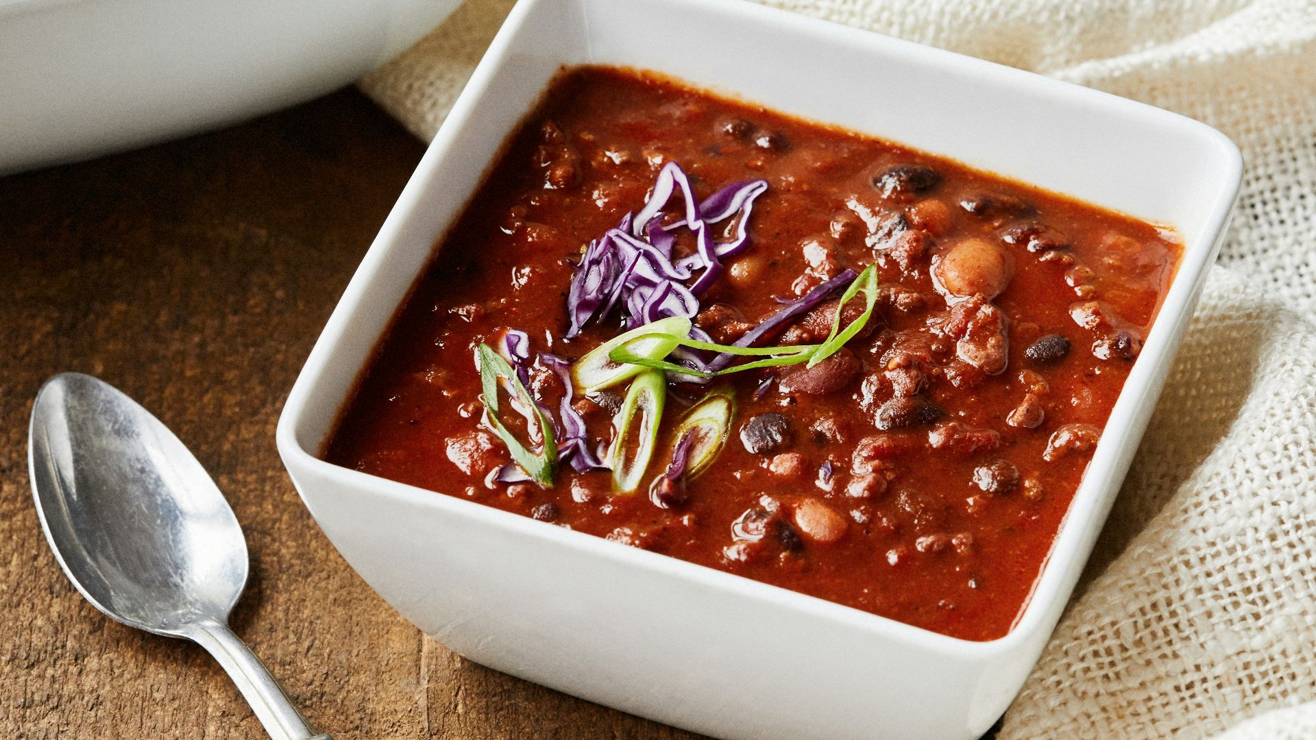 two bowls of chili and a spoon on a wooden table