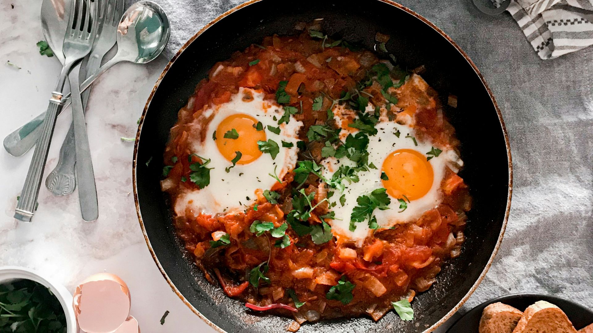 tomato soup on black cooking pan beside stainless steel fork and bread knife