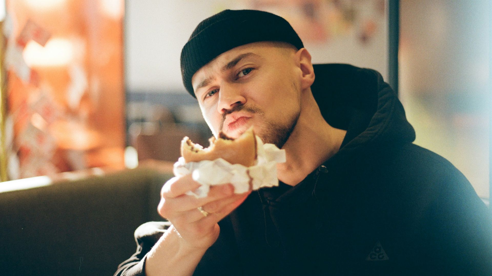 Man in black beanie eating a messy burger
