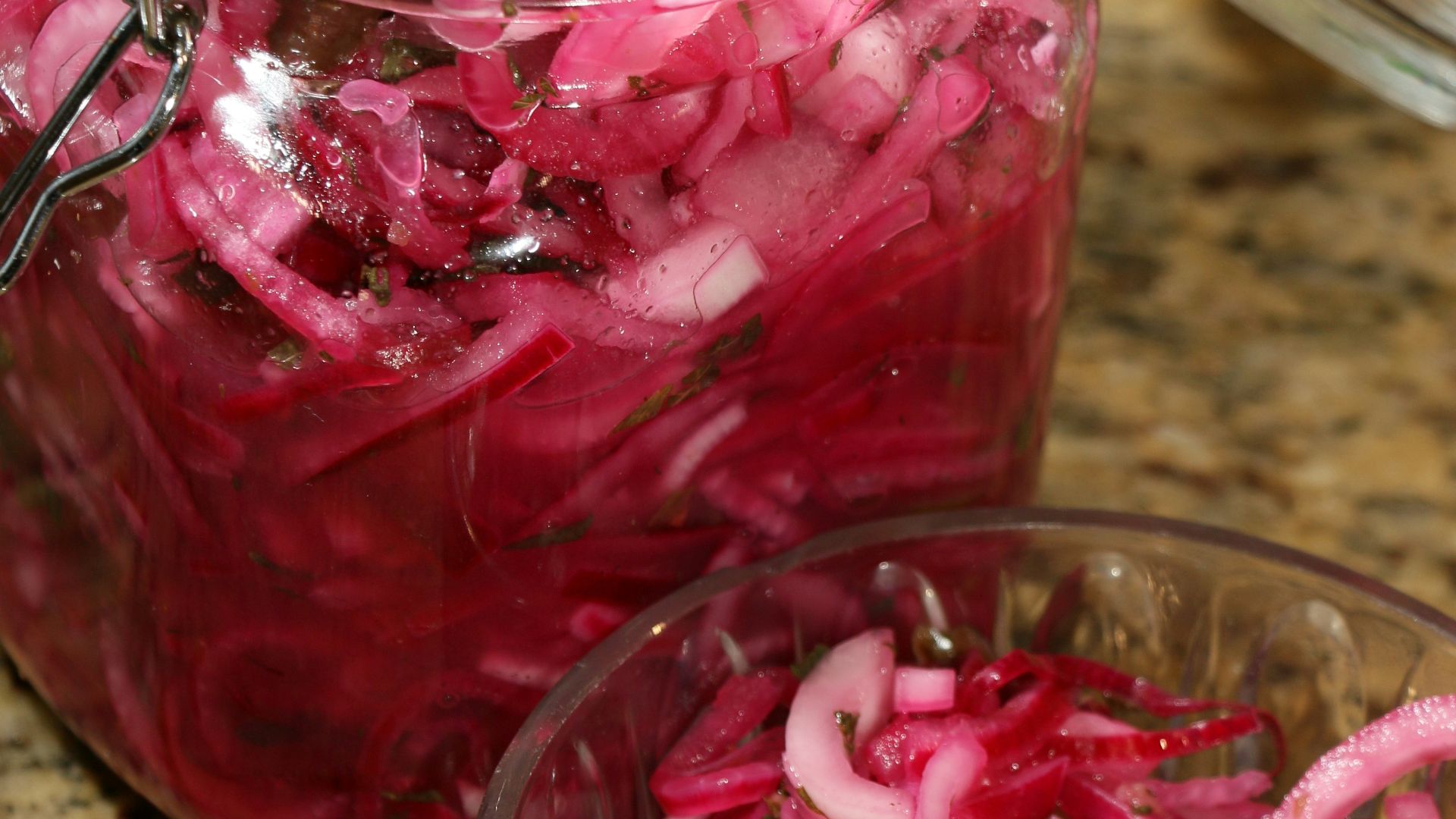a glass jar filled with red onions on top of a counter