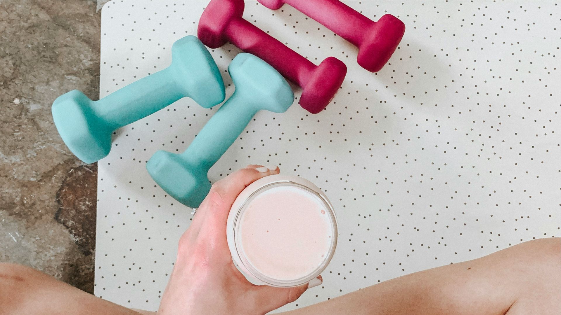 person holding white liquid filled cup above two pairs of dumbbells