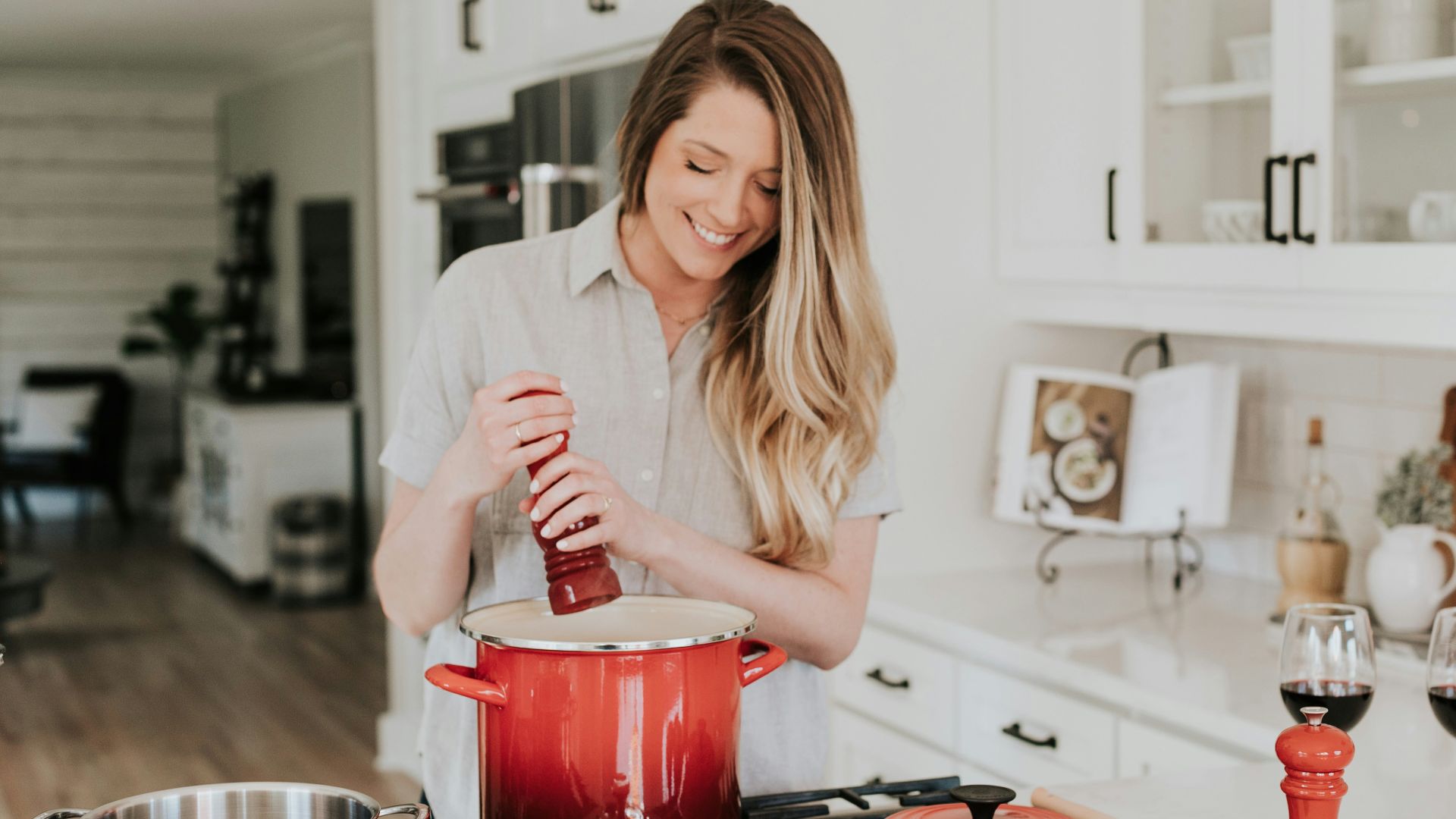 smiling woman standing and putting pepper on stock pot