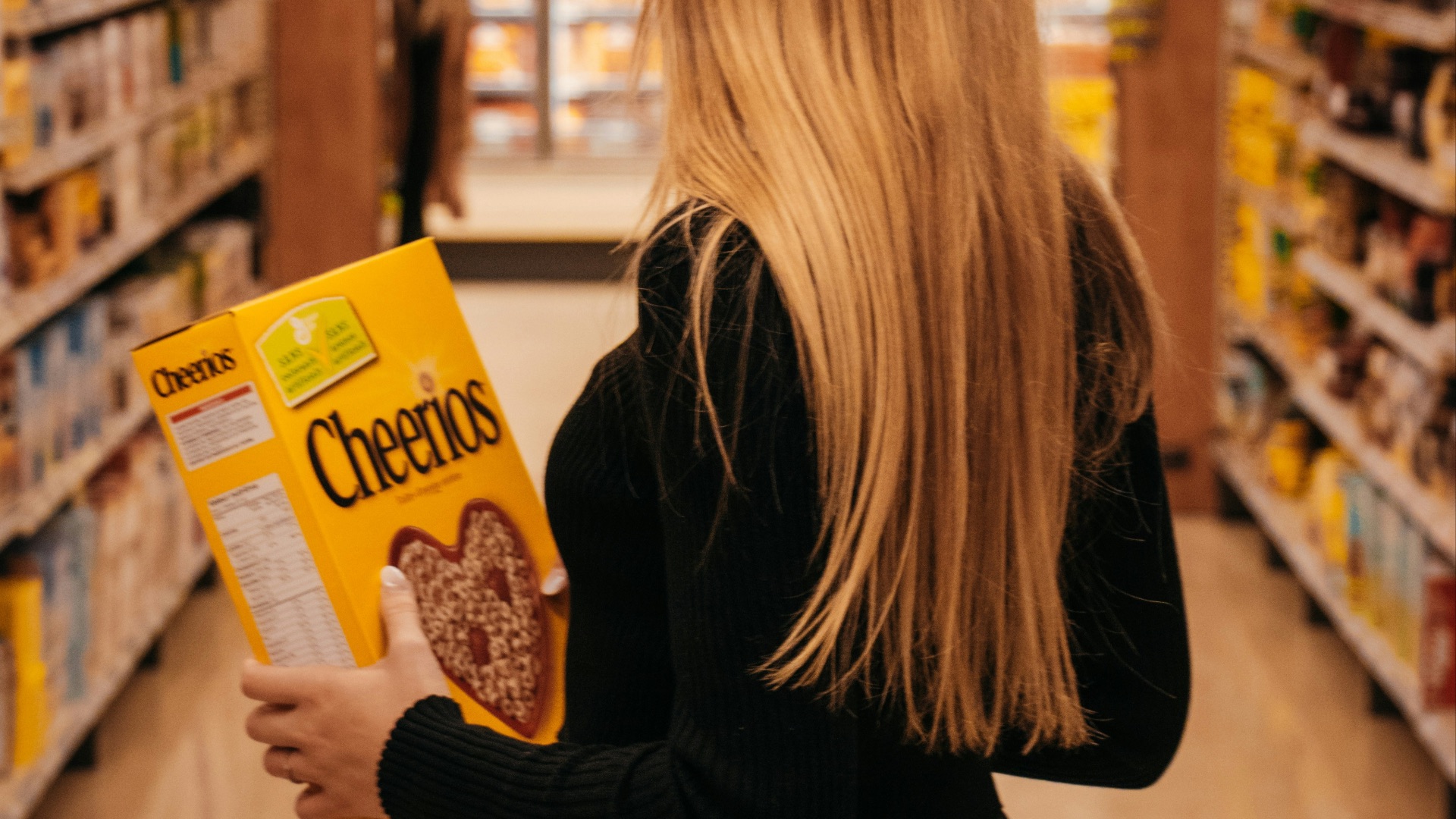 woman wearing black long-sleeved shirt holding Cheerios cereal box standing