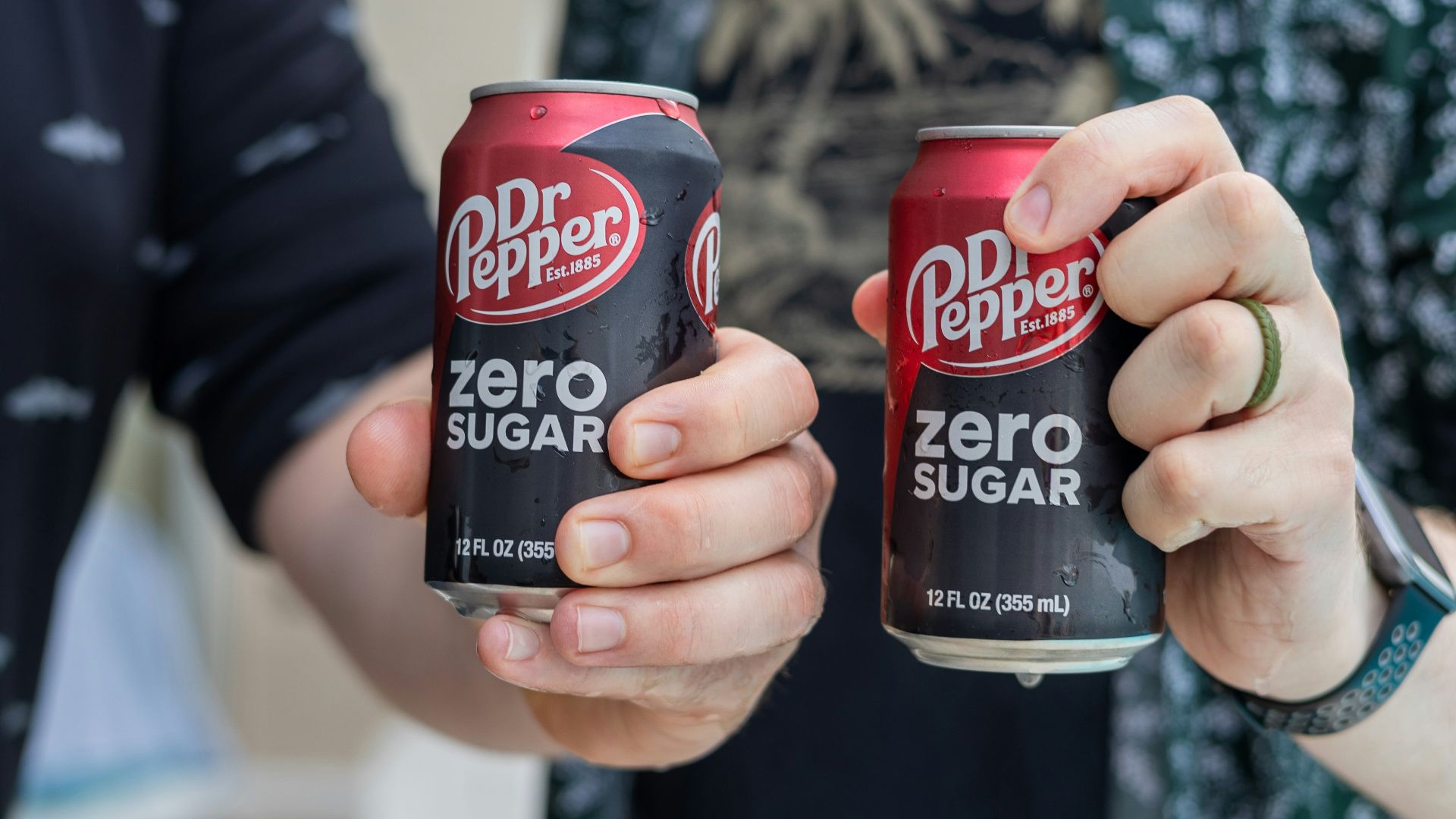 Two people are holding cans of dr. pepper zero sugar.