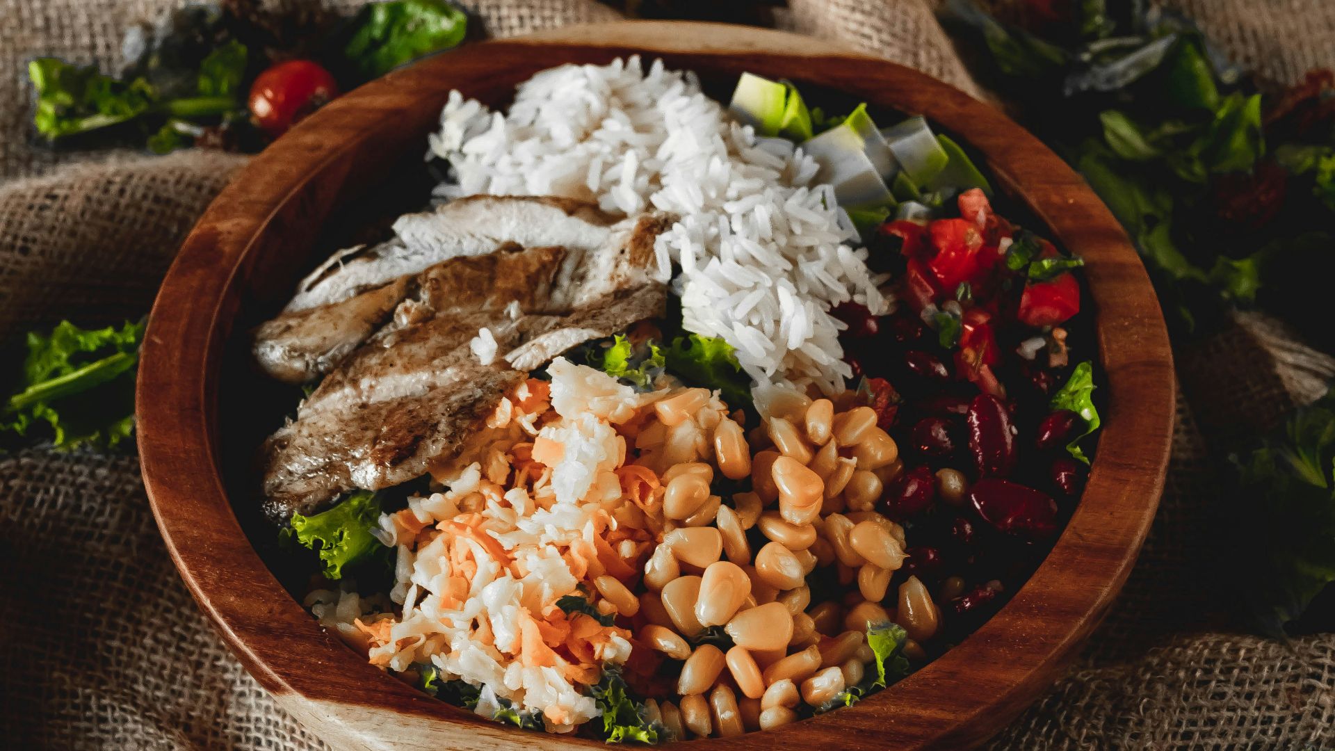 A wooden bowl filled with rice, chicken, and salad.
