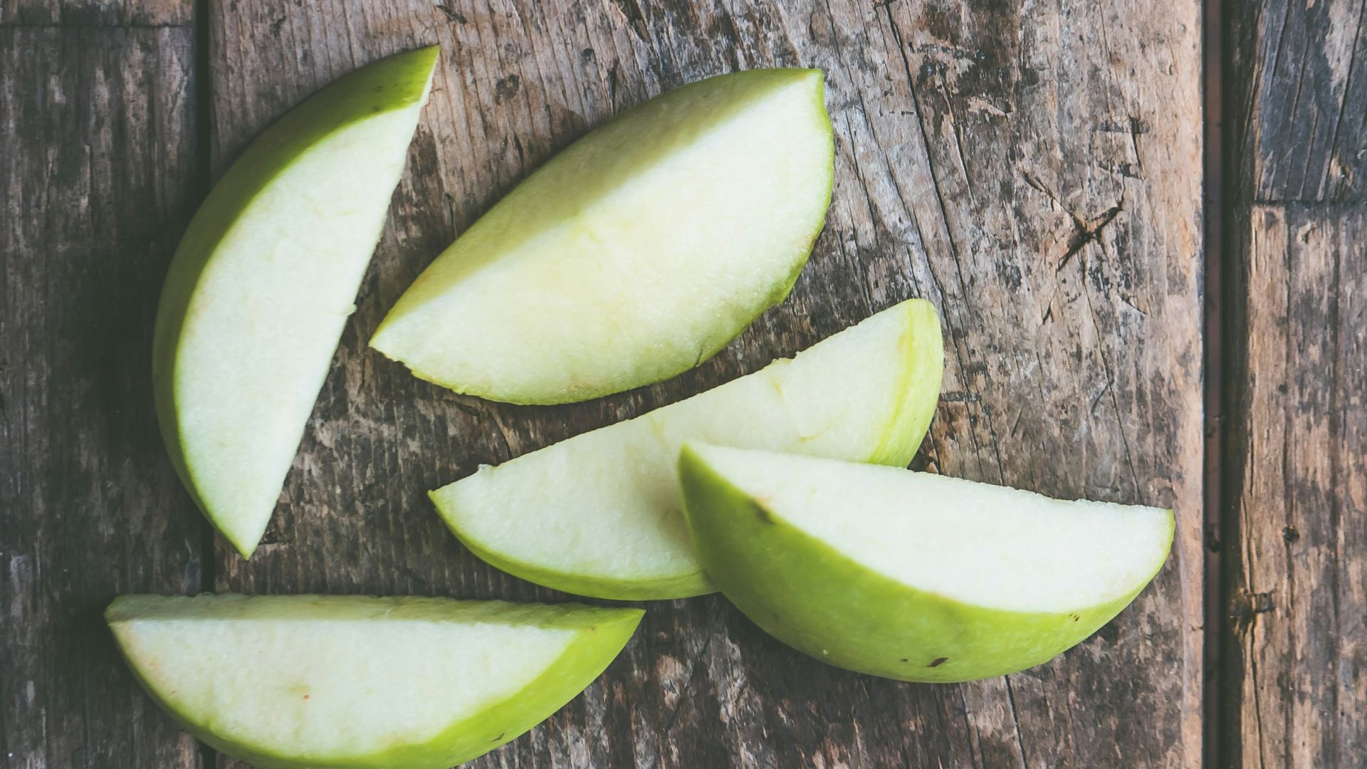 five green apple slices on brown wooden panel