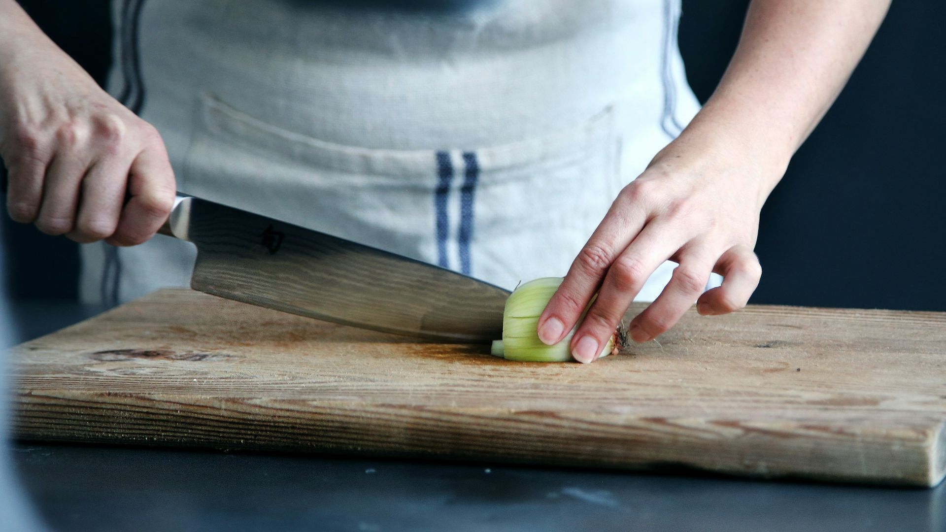 person slicing green vegetable on chopping board