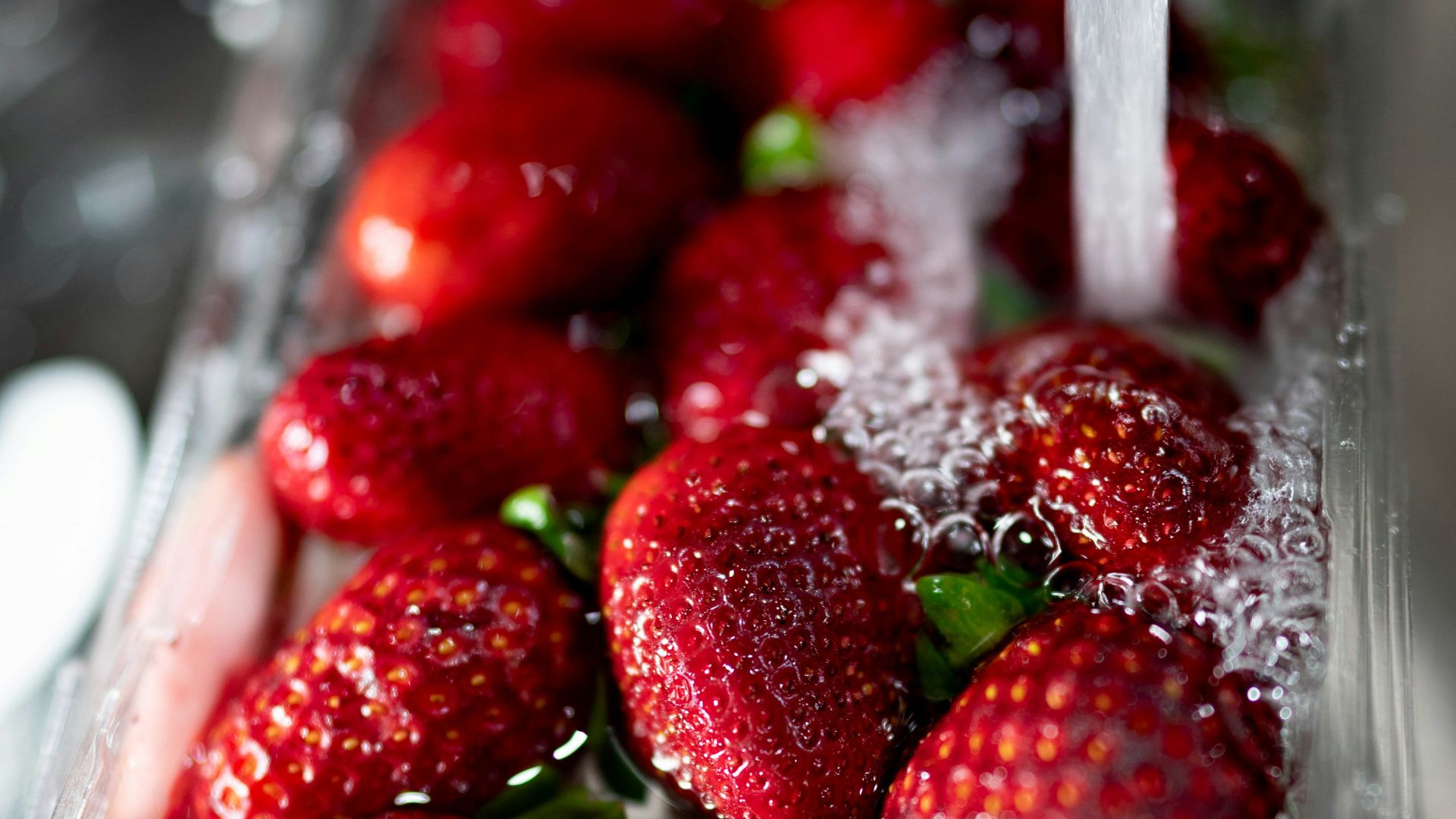 water poured into red strawberries in plastic tray