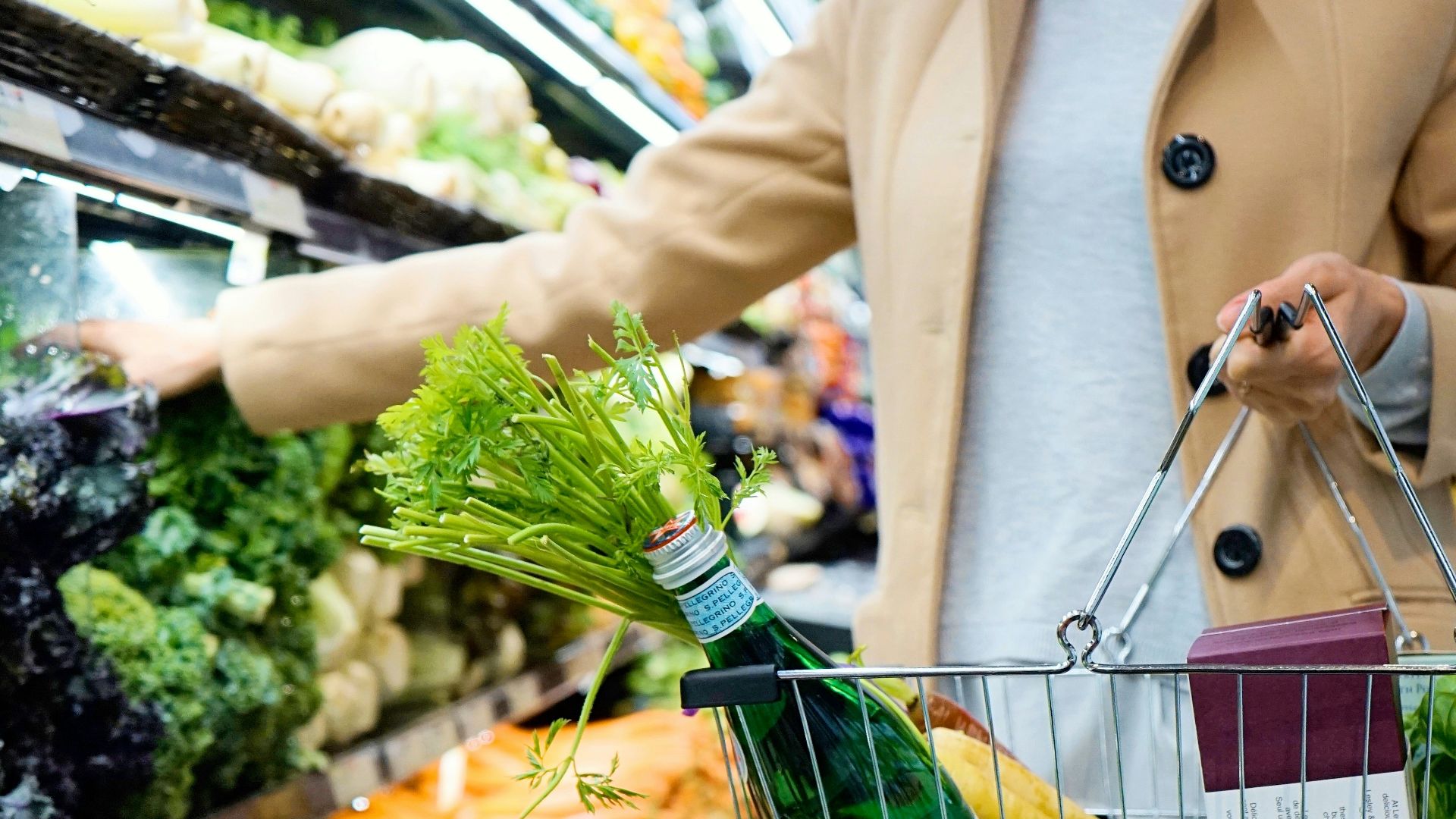 woman in white coat holding green shopping cart