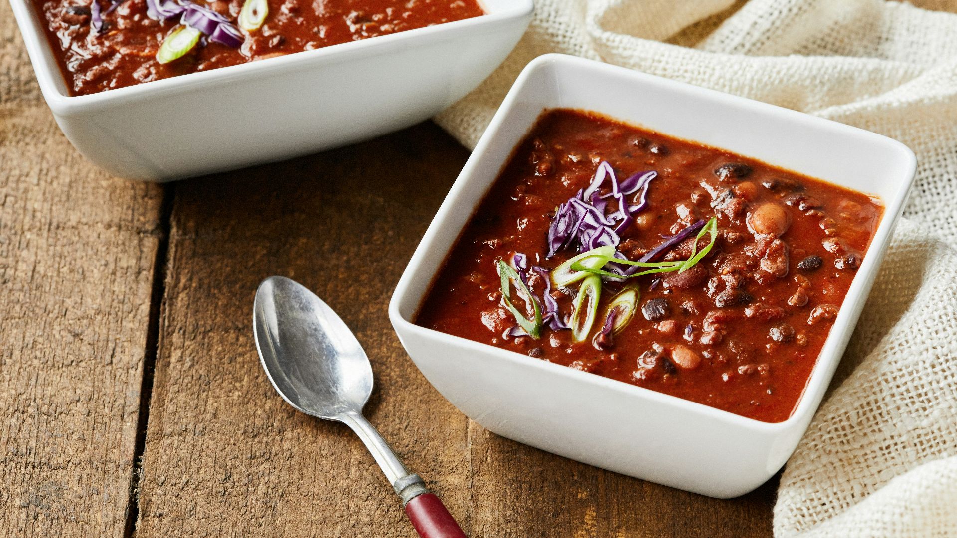 two bowls of chili and a spoon on a wooden table