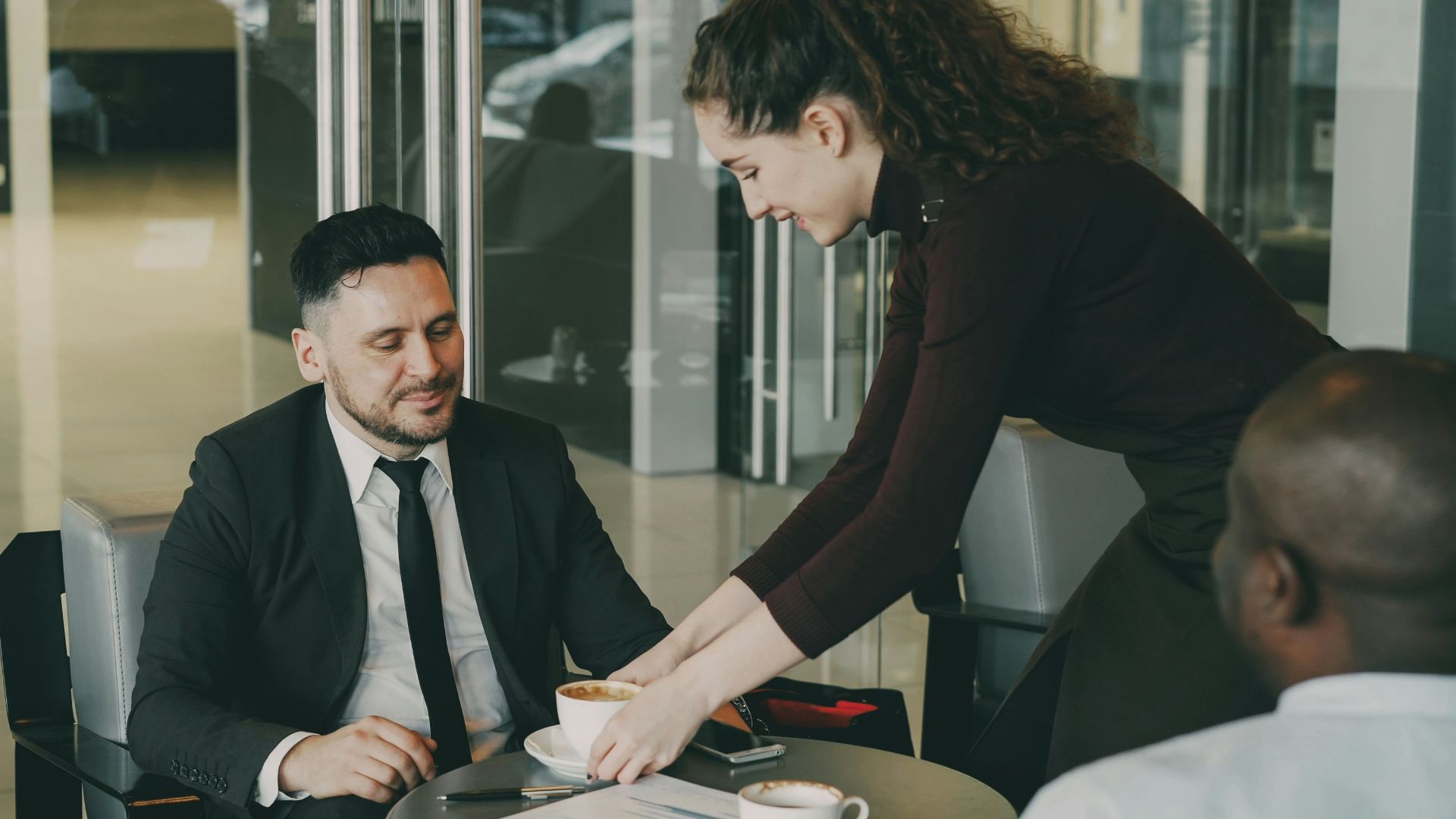 Waitress serving coffee to two businessmen in cafe.