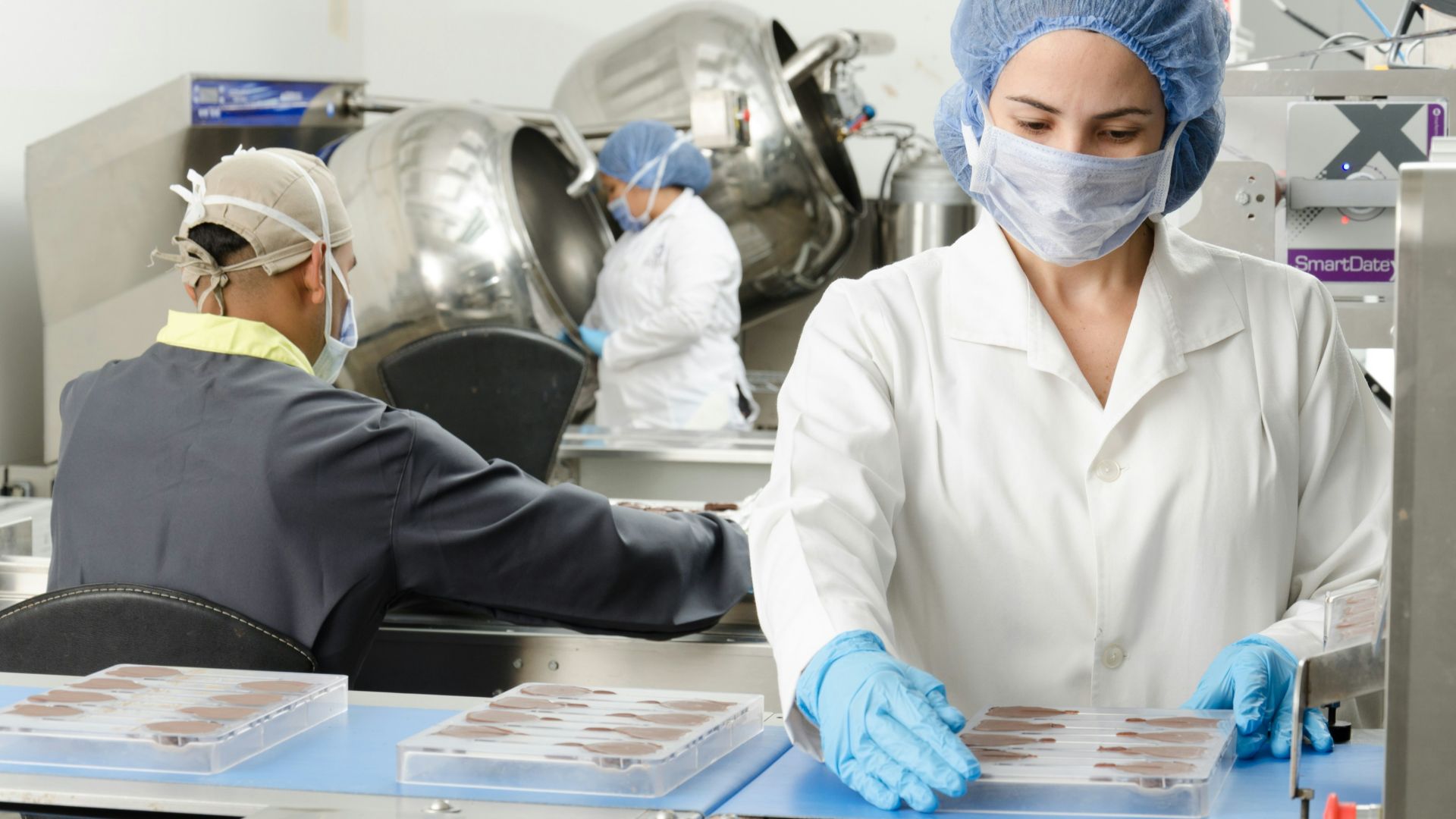 three people inside factory wearing masks and coats