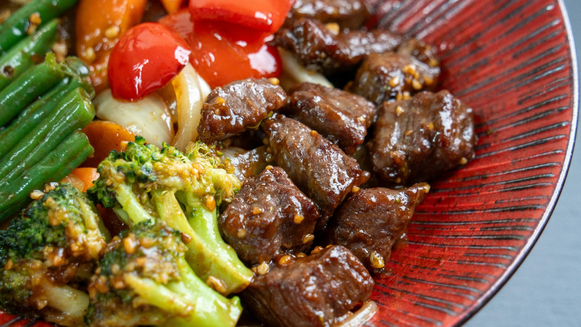 Beef and broccoli stir-fry with vegetables on a red plate