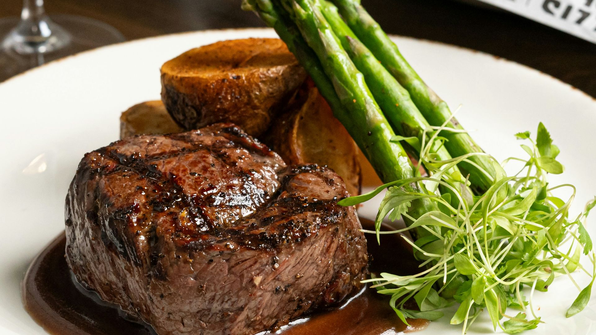 a plate of steak and asparagus with a glass of wine