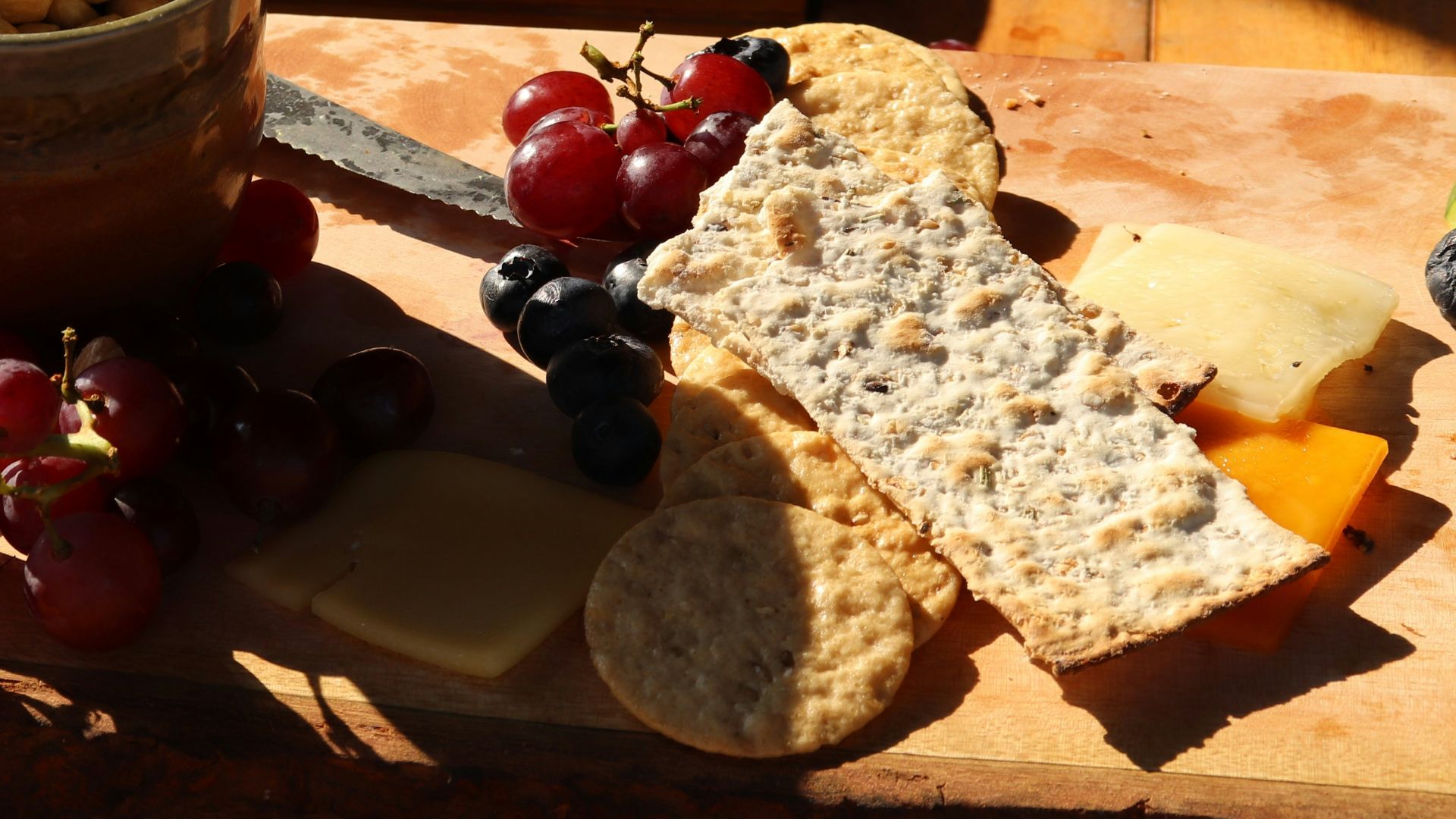 a wooden cutting board topped with grapes and crackers
