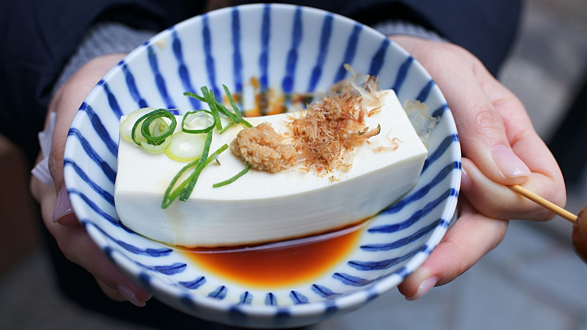 person holding white and blue ceramic plate with rice and sliced cucumber