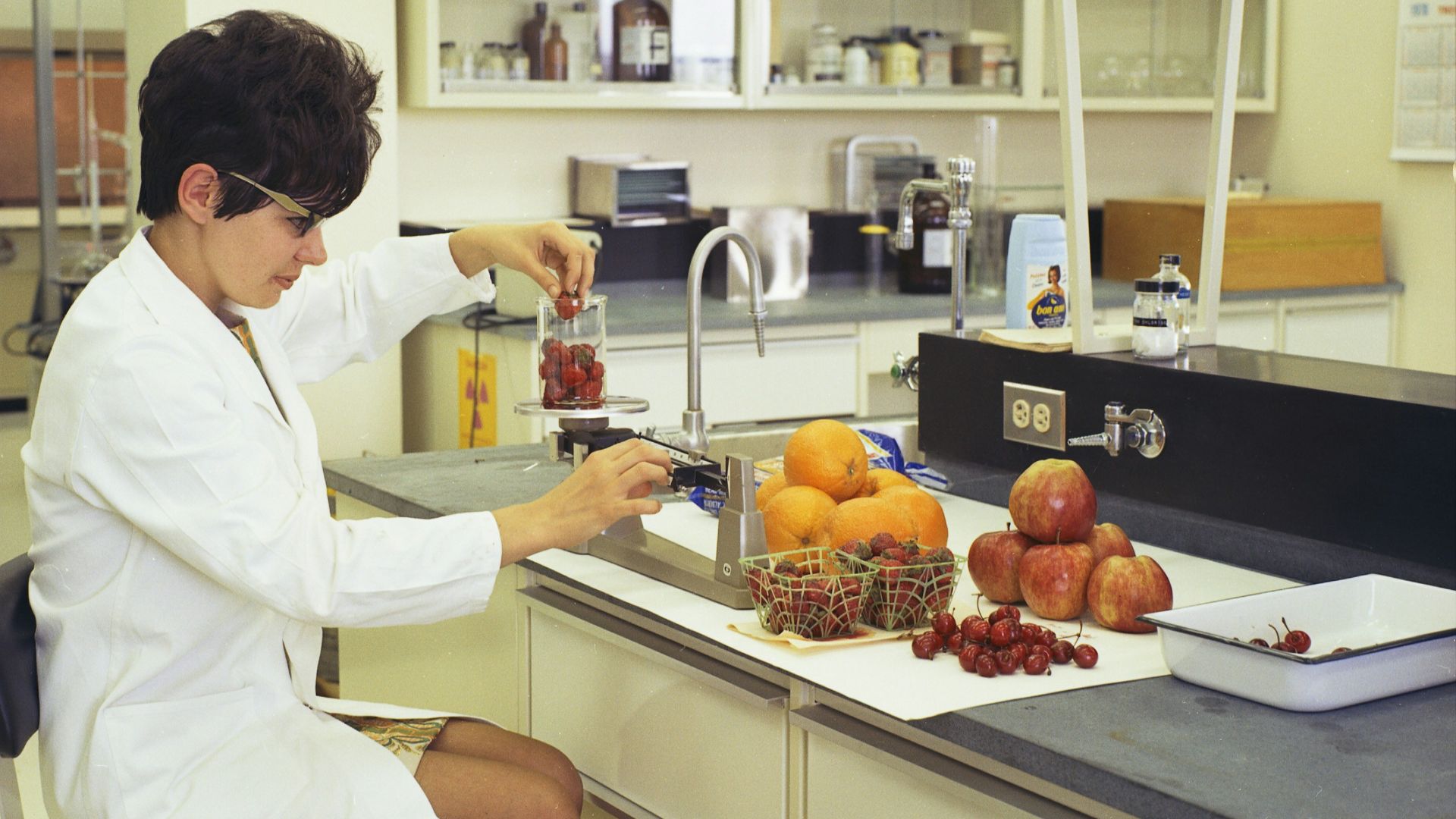 a woman in a white lab coat sitting at a counter in front of a sink