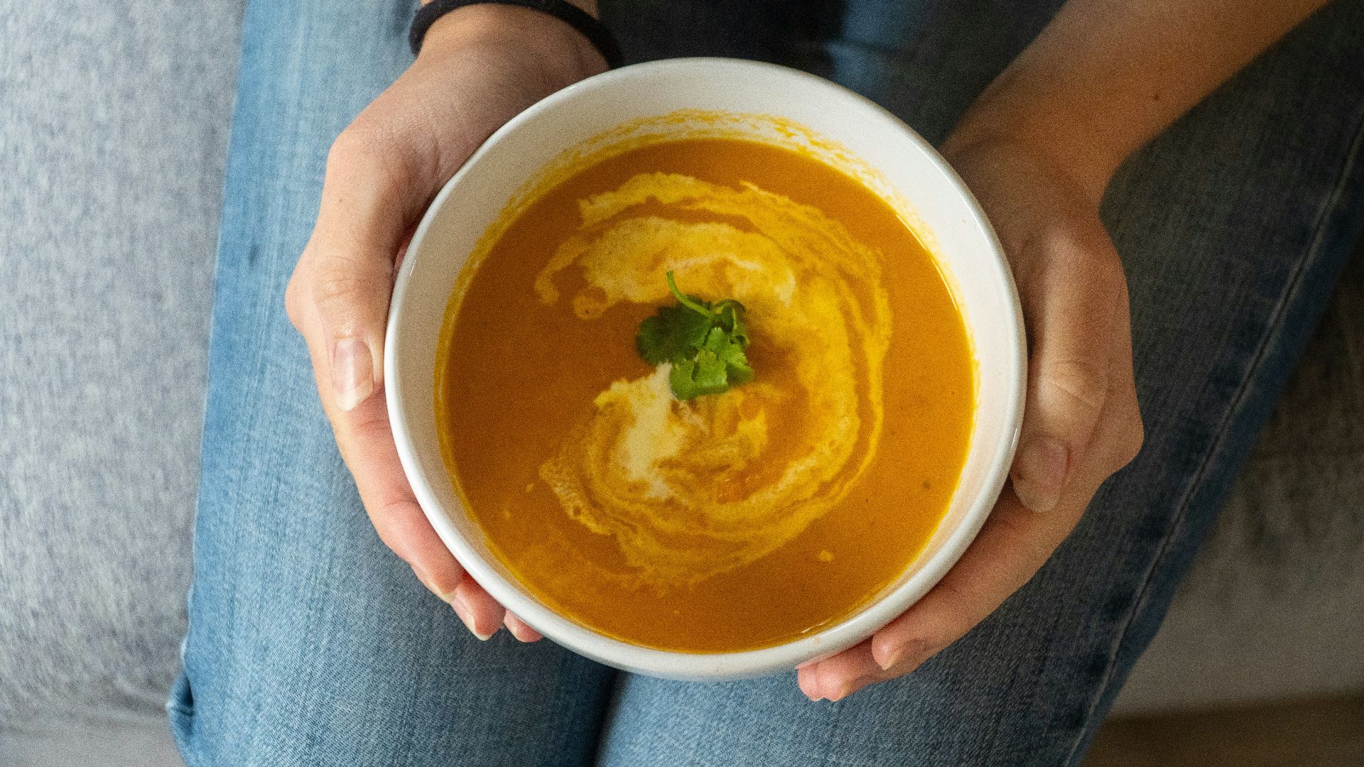Bowl of creamy orange soup with swirl and herb garnish