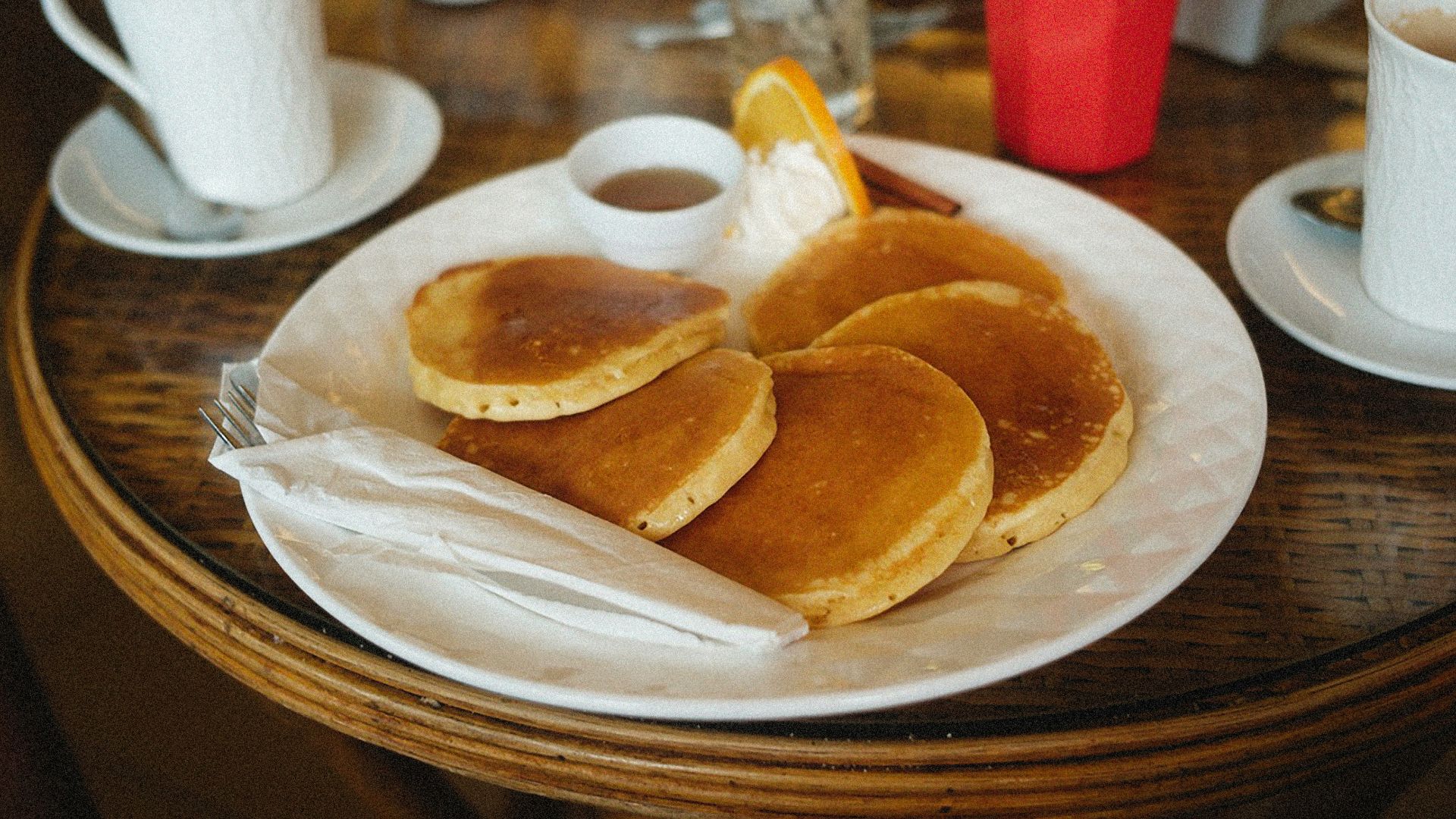 a white plate topped with pancakes next to cups of coffee