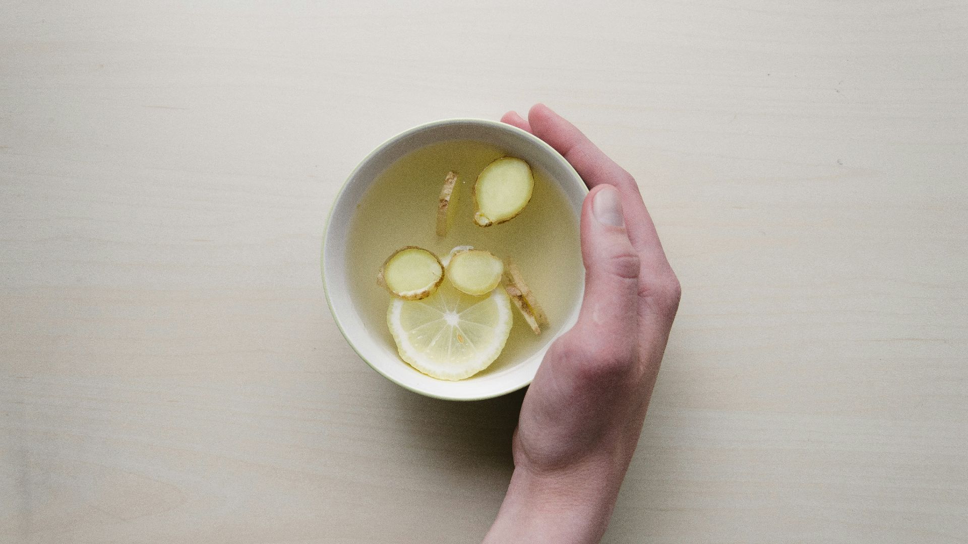 person holding white bowl with sliced lime and ginger inside
