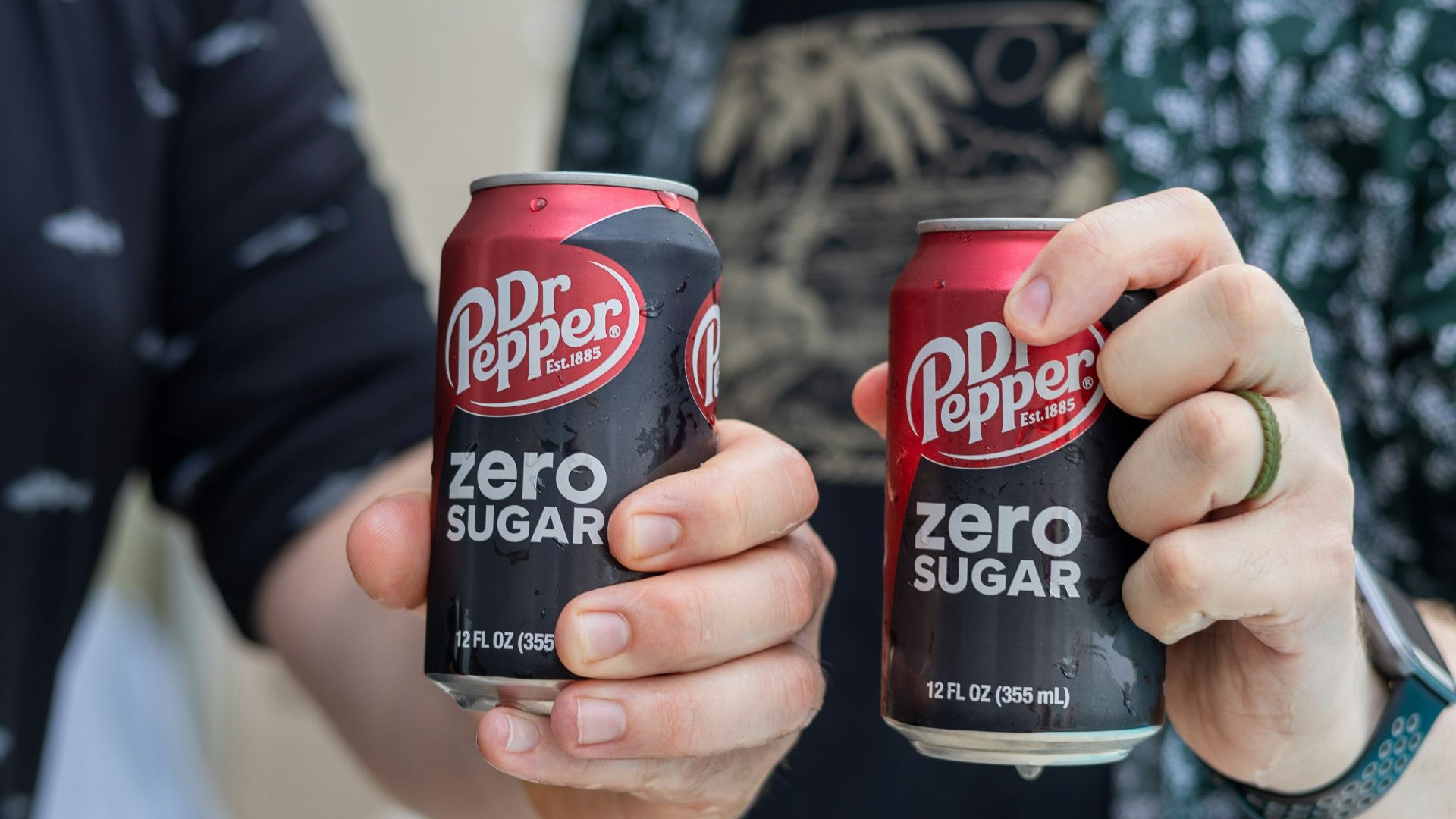 Two people are holding cans of dr. pepper zero sugar.