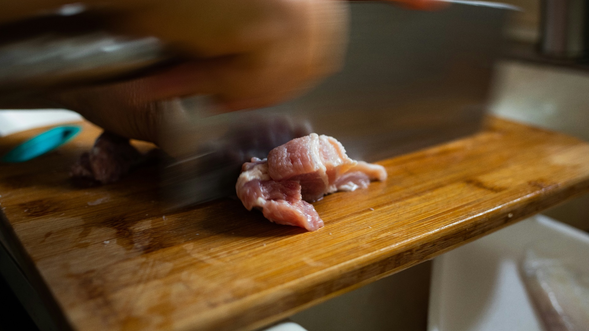 person slicing raw meat on brown wooden chopping board