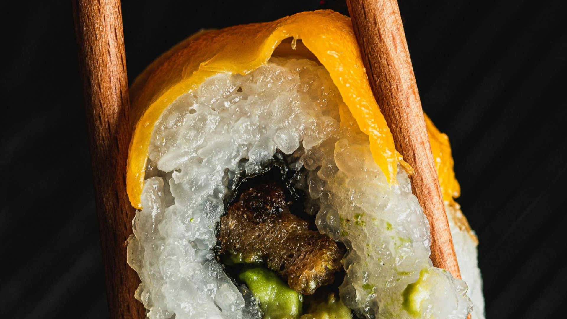 Chopsticks holding a sushi roll with avocado and eel.