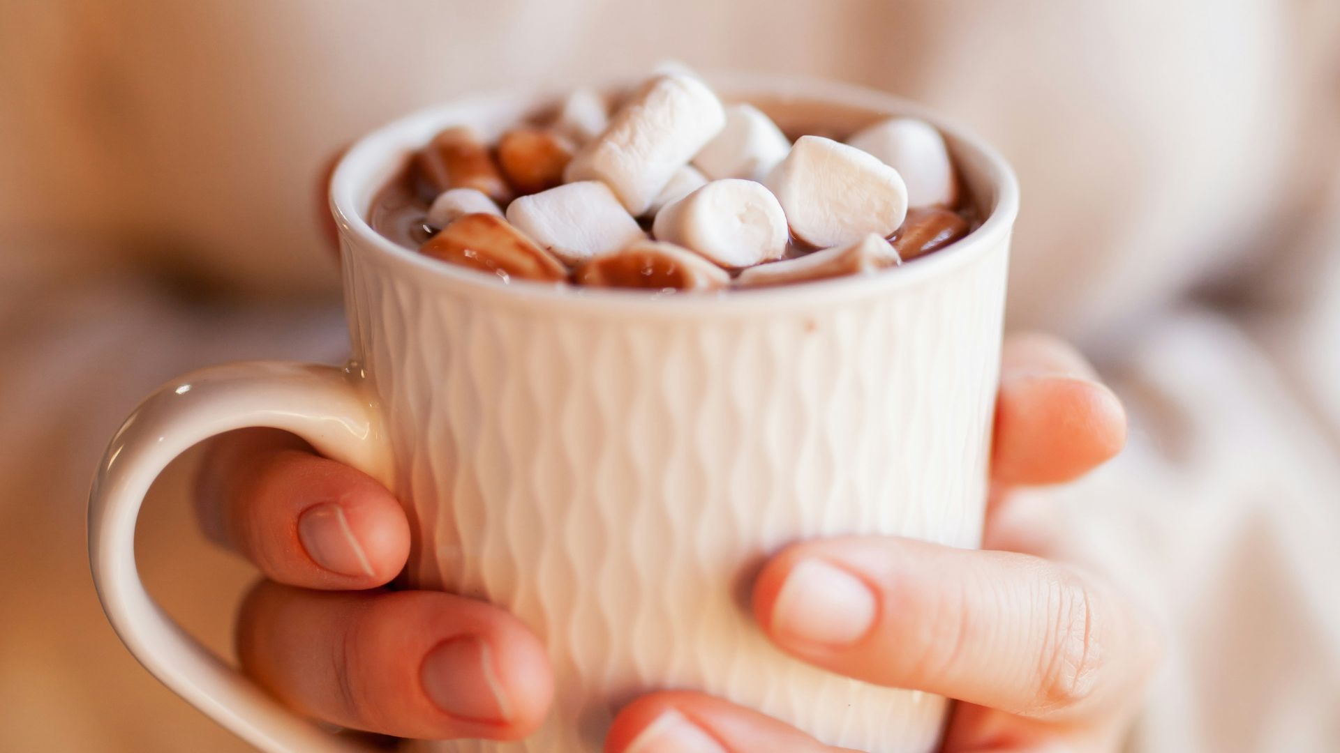 person holding white ceramic mug with brown and white beans