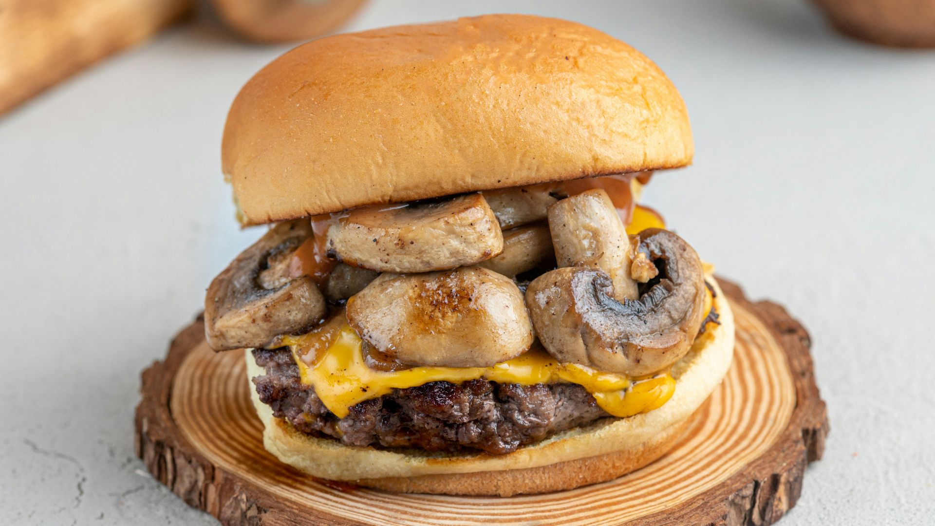 a cheeseburger with mushrooms on a wooden plate