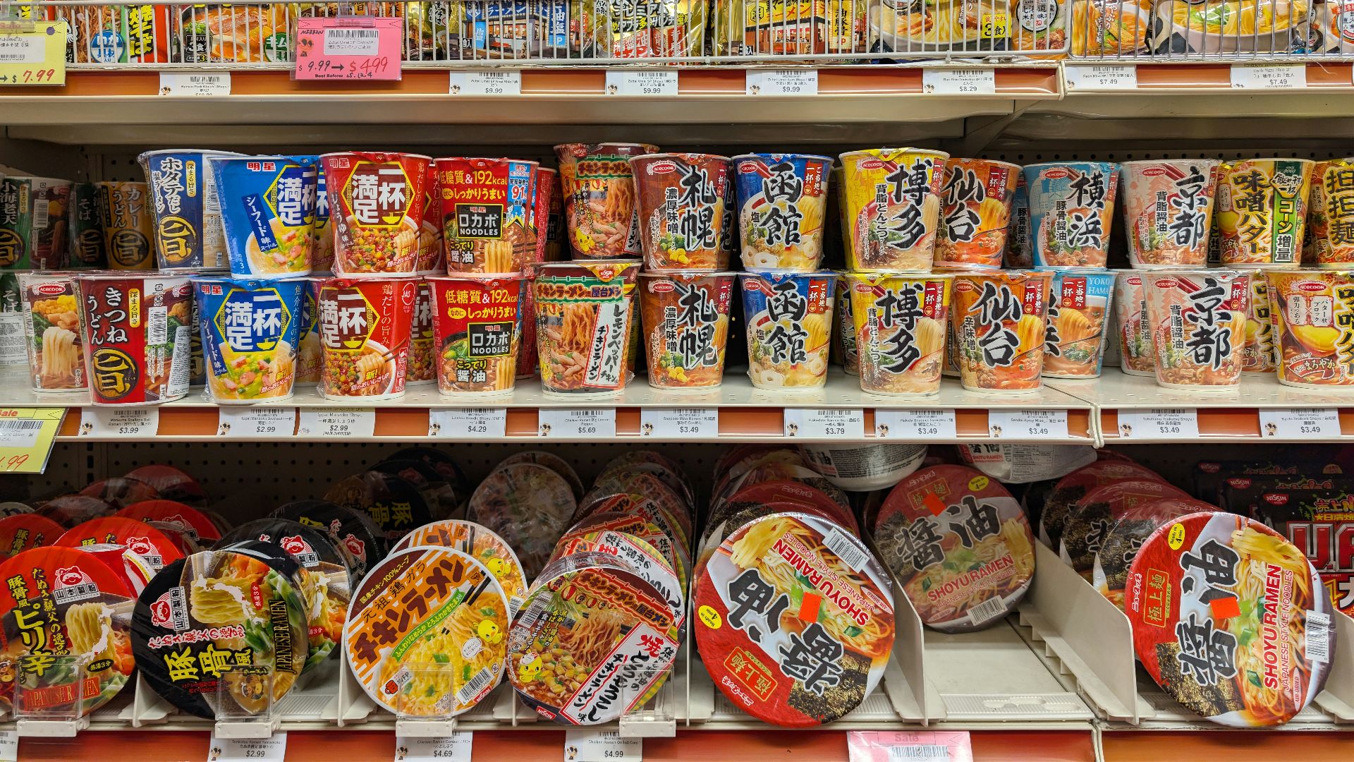 Shelves stocked with various instant noodle cups and packets.