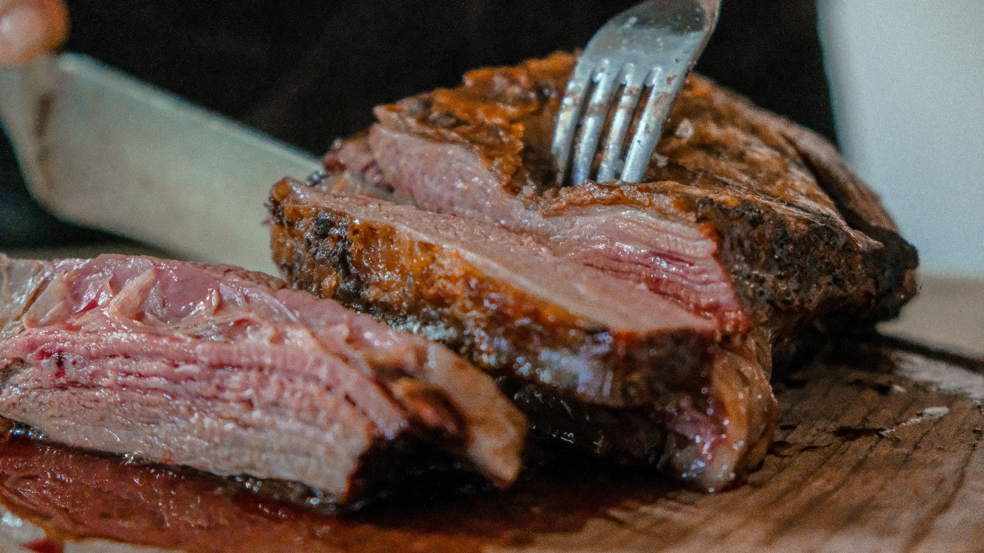 person slicing a meat on brown wooden board