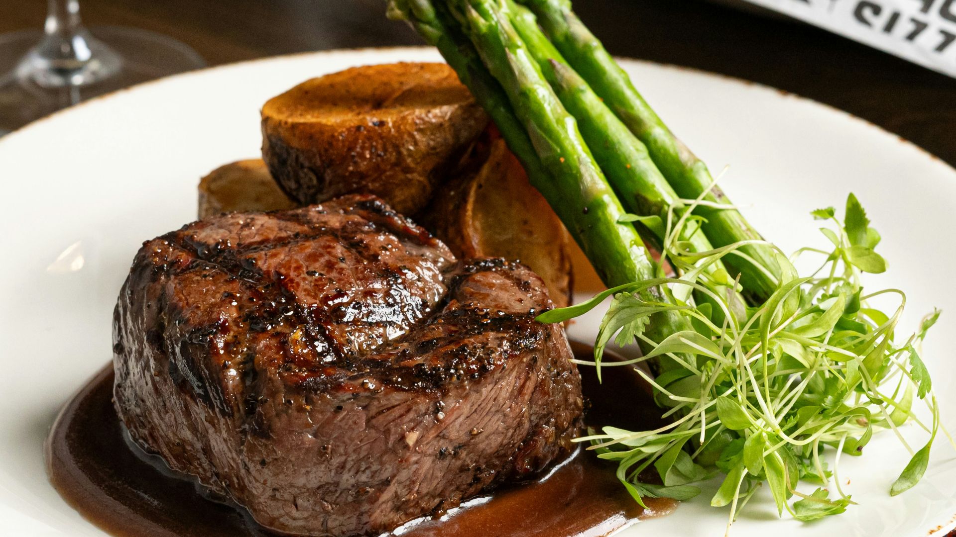 a plate of steak and asparagus with a glass of wine