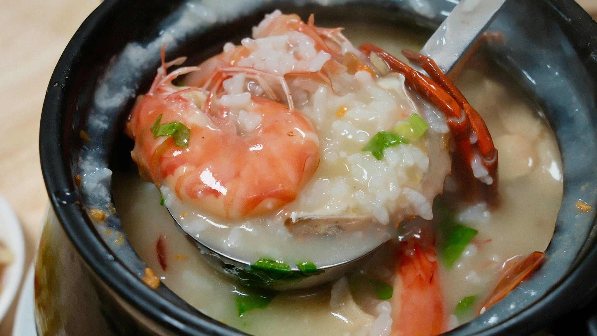 A steaming bowl of congee with shrimp and garnishes