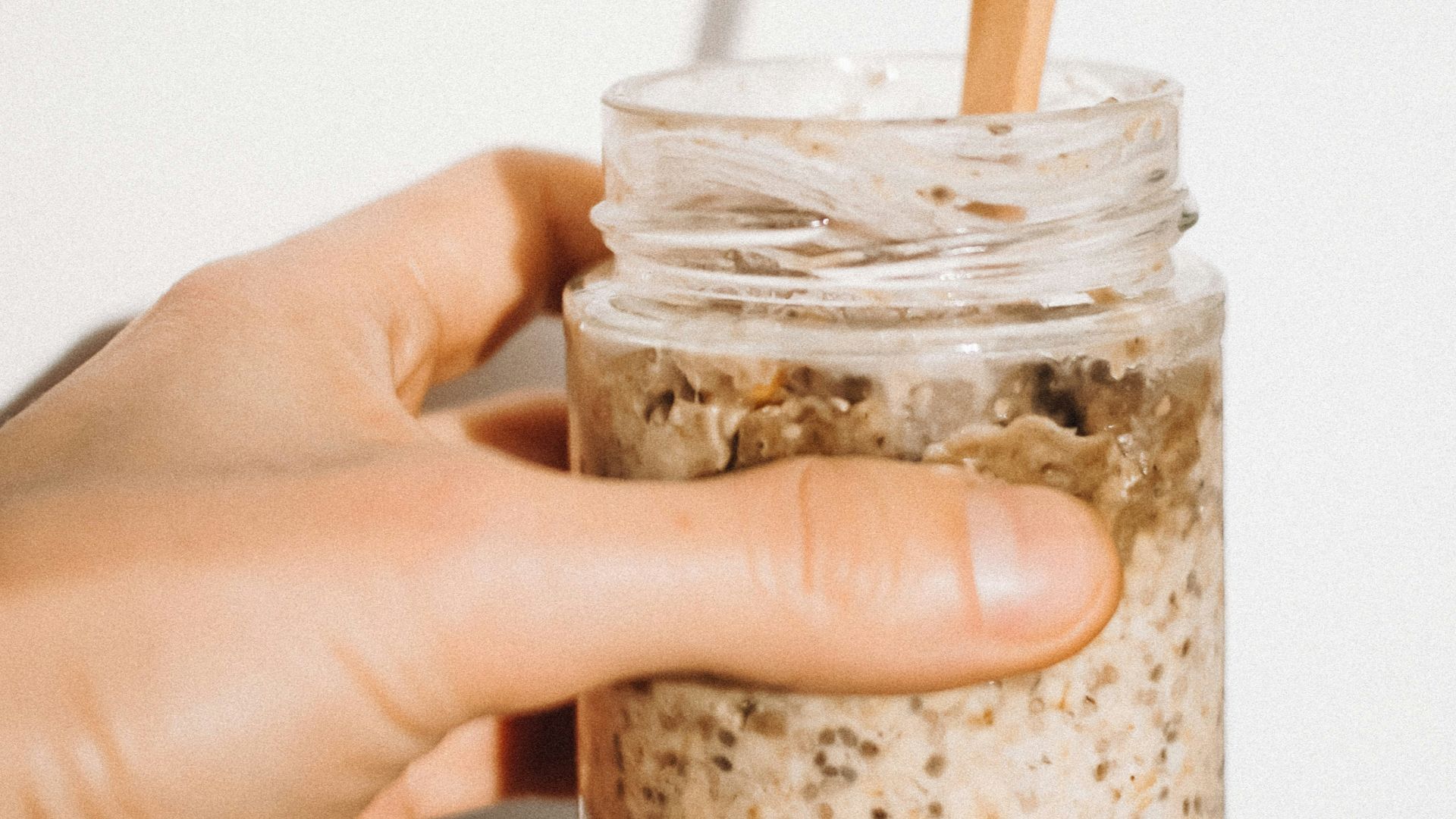 a person holding a jar of food with a wooden spoon in it