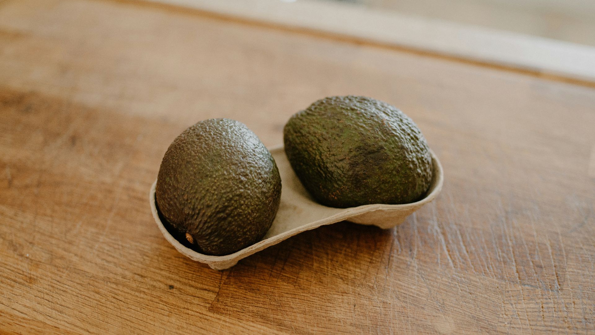 Two avocados in a holder on a wooden surface