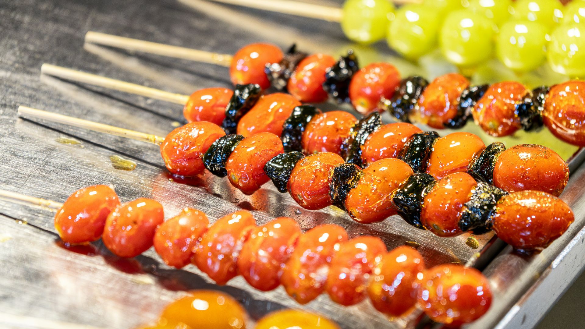 Candied fruits on skewers, including tomatoes and grapes.