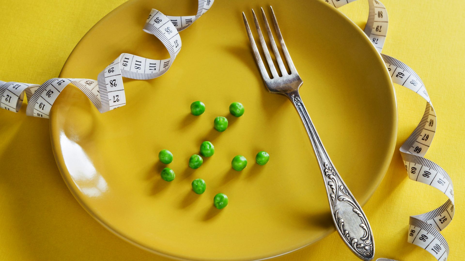 a plate with a fork, measuring tape and green peas
