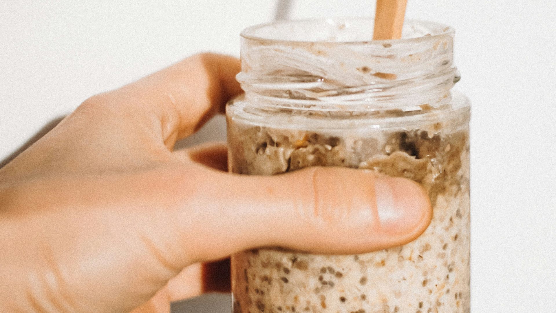 a person holding a jar of food with a wooden spoon in it