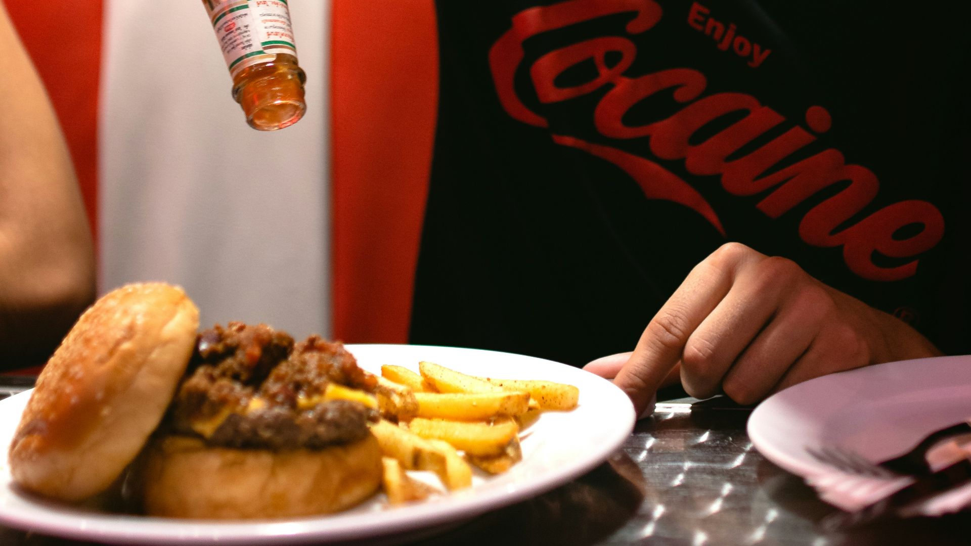 man pouring sauce on burger and fries