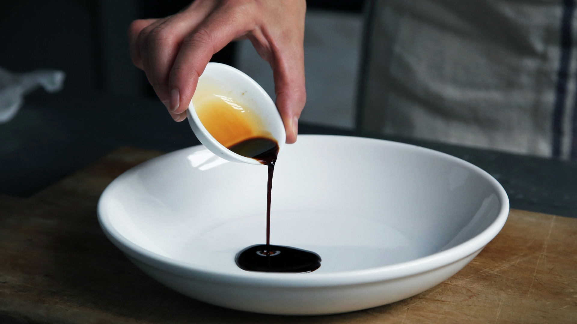 person dripping black liquid from small white ceramic bowl to big white ceramic bowl