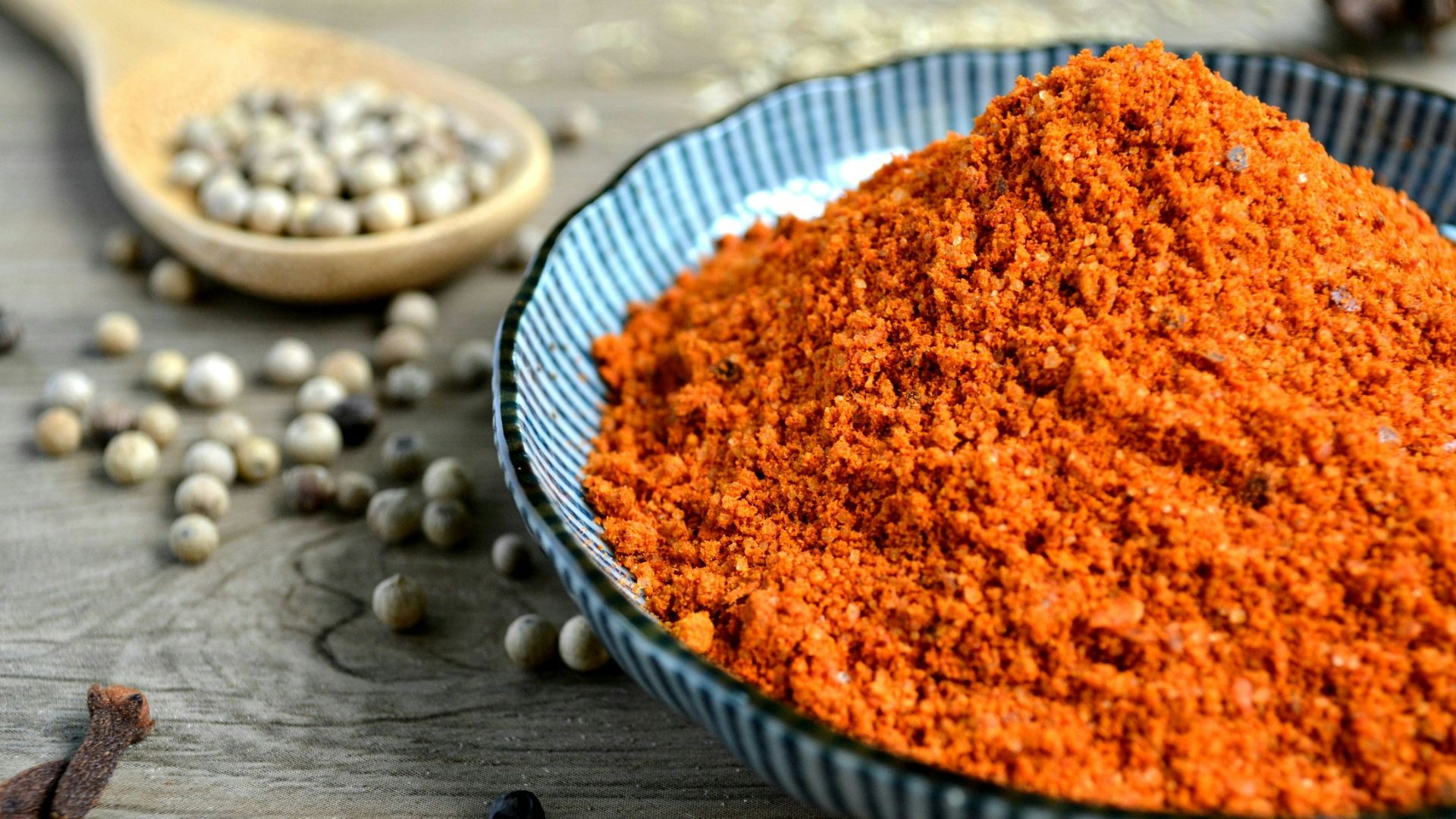 red spices on blue bowl with peppers scattered on table