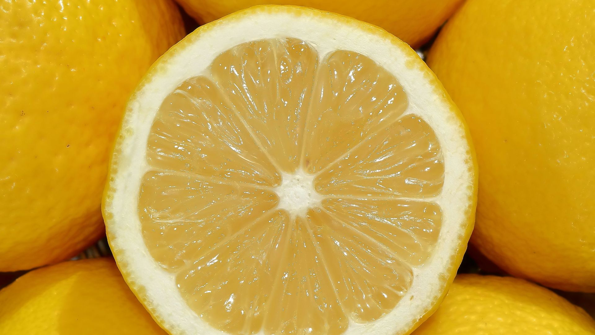A close-up of a sliced lemon surrounded by whole lemons
